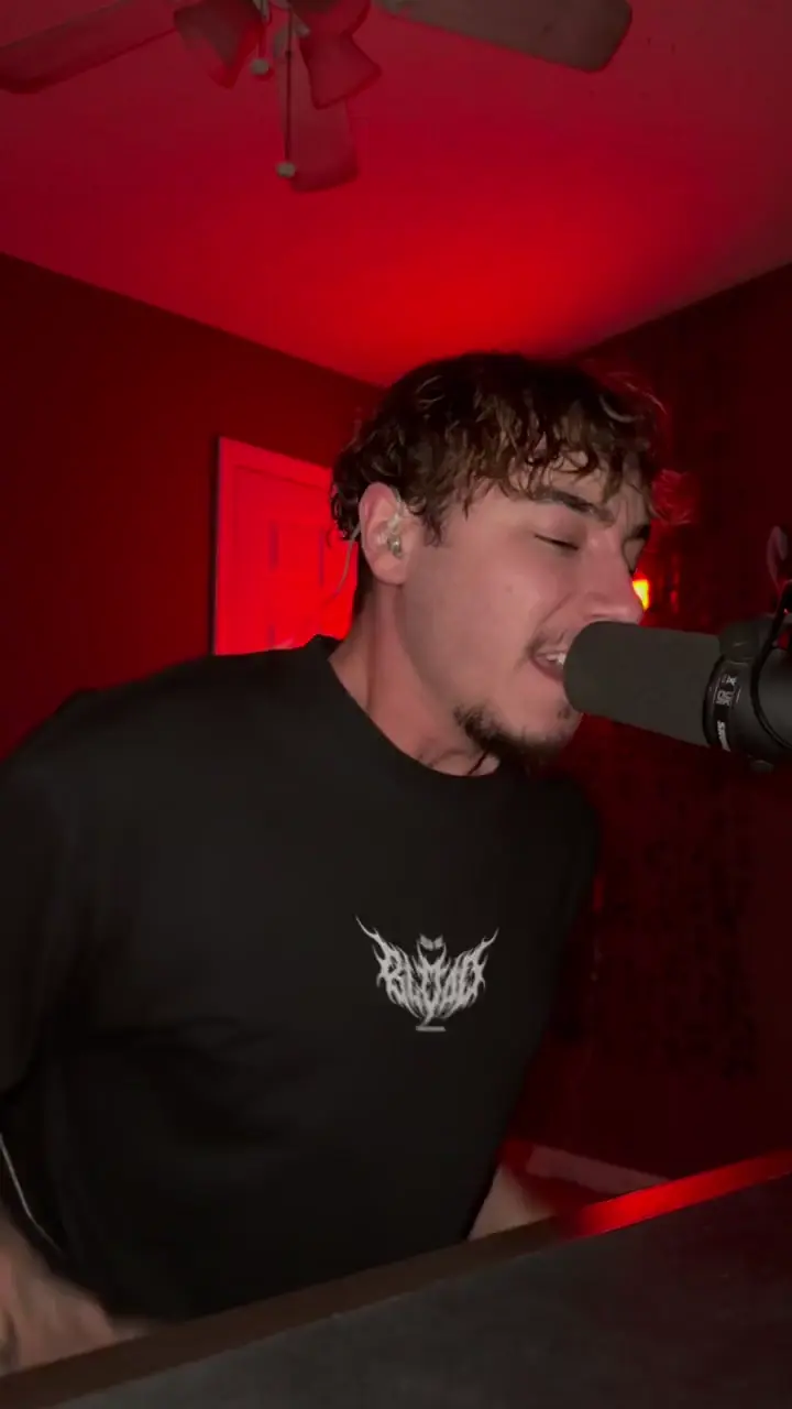 amen beside a microphone in his red-lit recording room