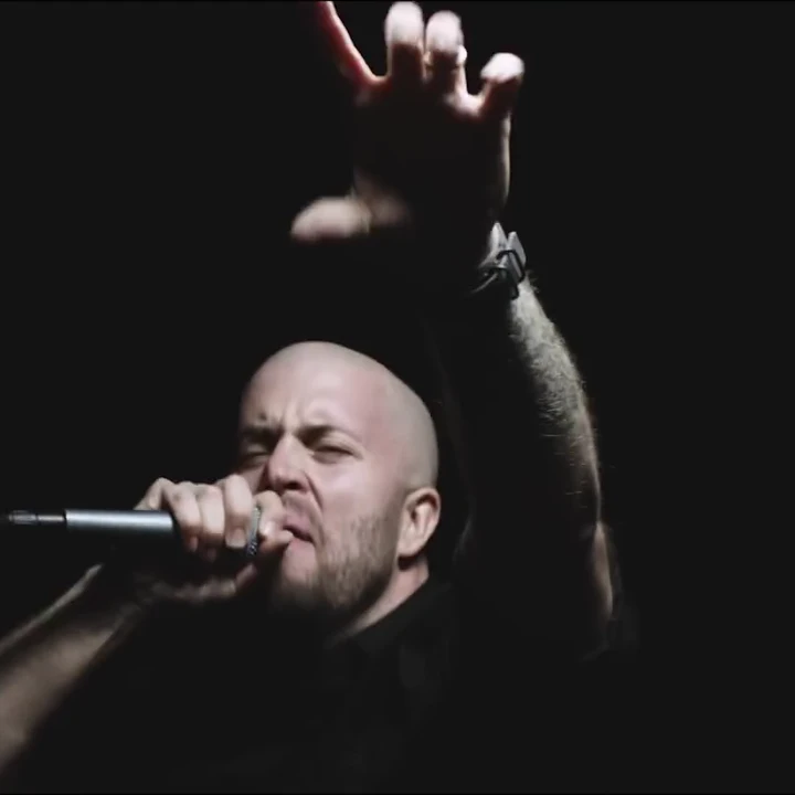 Andrew Schwab singing into a microphone with one arm raised onstage