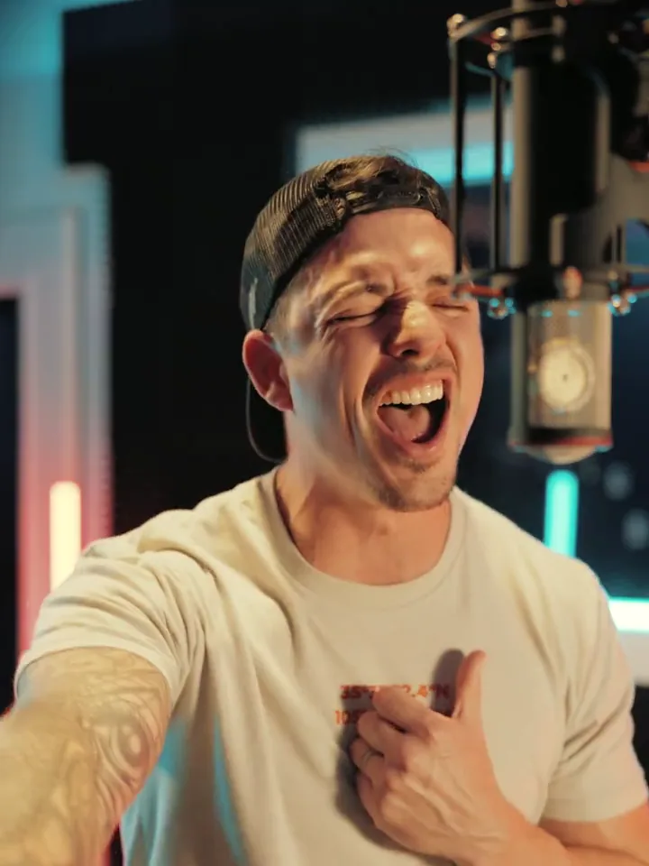 Tony Veda singing at a studio microphone in a backward cap