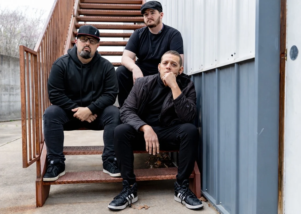 XIII Minutes seated together on an outdoor staircase beside a metal building