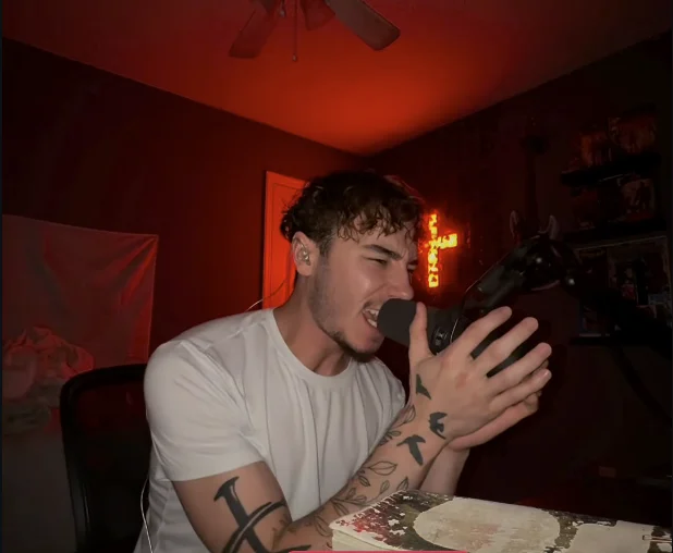 amen screaming into a microphone in a red-lit room with a cross behind him